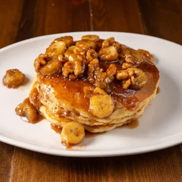 Stack of pancakes topped with caramelized bananas, walnuts, and syrup on a white plate.