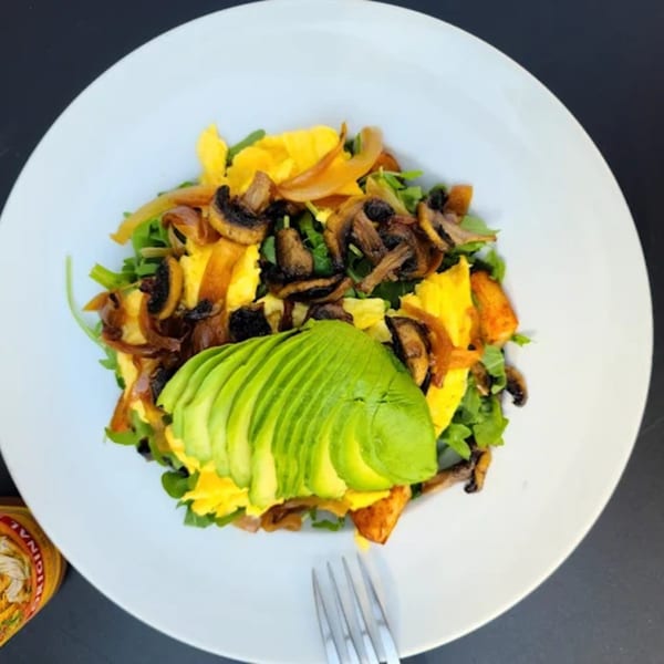 City Kitchen's breakfast scramble with eggs, mushrooms, onions, arugula, and sliced avocado on a white plate.