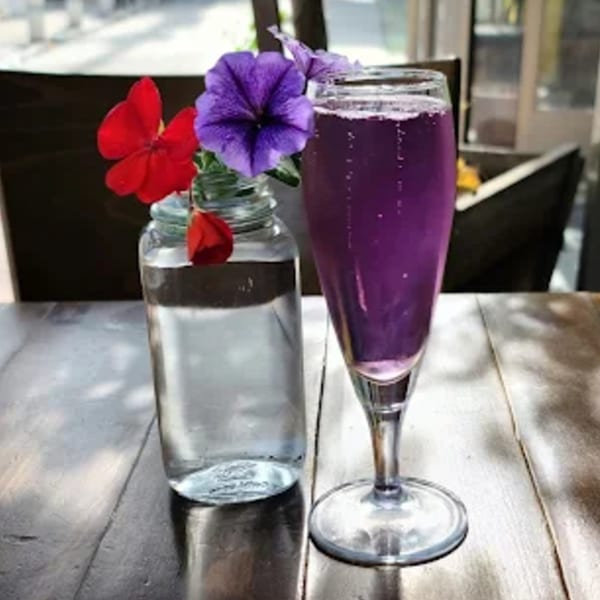A purple sparkling drink in a flute glass next to a vase with red and purple flowers.