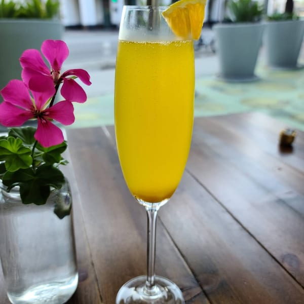A mimosa with an orange slice and a pink flower in a vase on a wooden table.