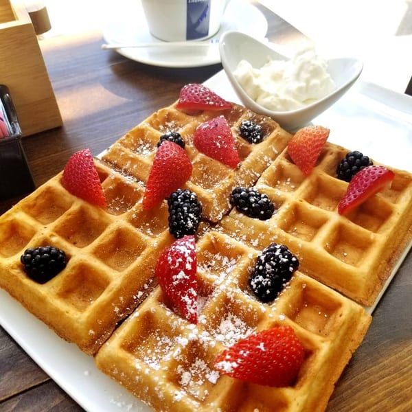 Golden waffles topped with strawberries, blackberries, powdered sugar, and a side of whipped cream.