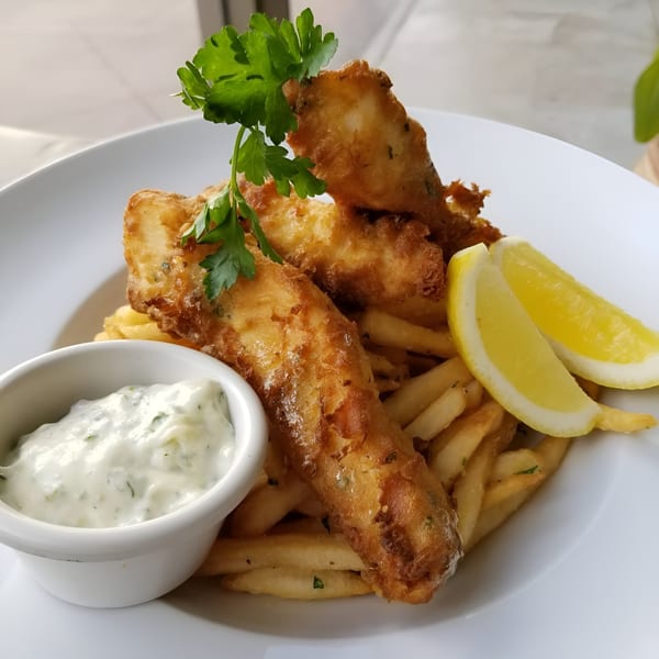 Golden-brown fish and chips with tartar sauce, lemon wedges, and parsley on a white plate.